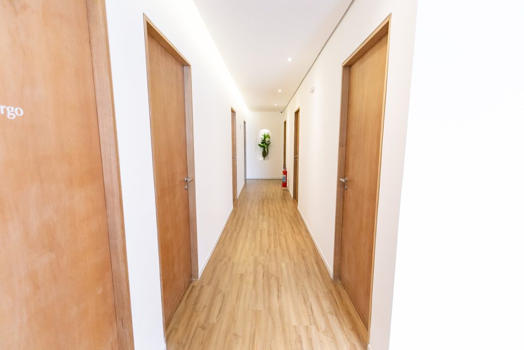 Corredor claro de consultórios da clínica, com portas de madeira e piso amadeirado