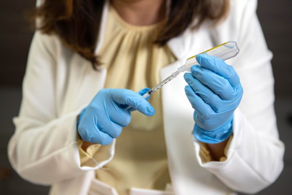 Mãos com luvas azuis aspiram o conteúdo de uma ampola com seringa antes de um procedimento injetável