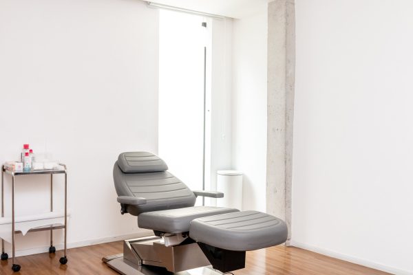 Sala de procedimentos da clínica: maca reclinável e carrinho de inox com frascos